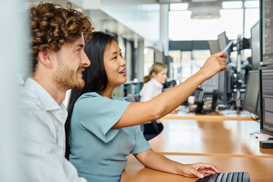 two people looking at screens Two people sitting at a desk while they point at the screen